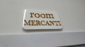 A sign with the words "ROOM MERCANTI" in gold lettering on a white background.