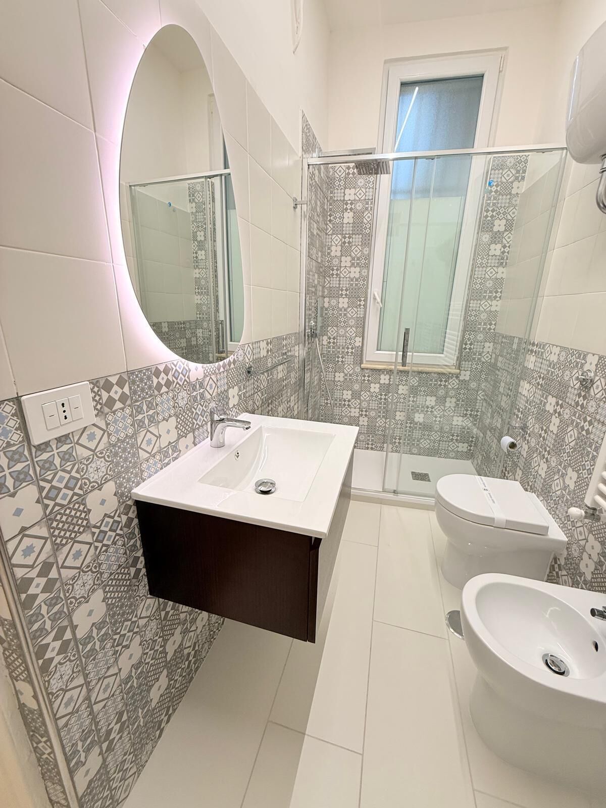 Un baño moderno con un lavabo blanco, un tocador de madera oscura, un inodoro y una zona de ducha.