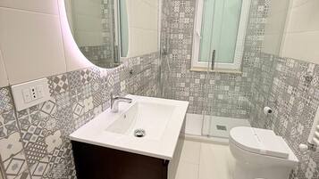 Un baño moderno con un lavabo blanco, un tocador de madera oscura, un inodoro y una zona de ducha.