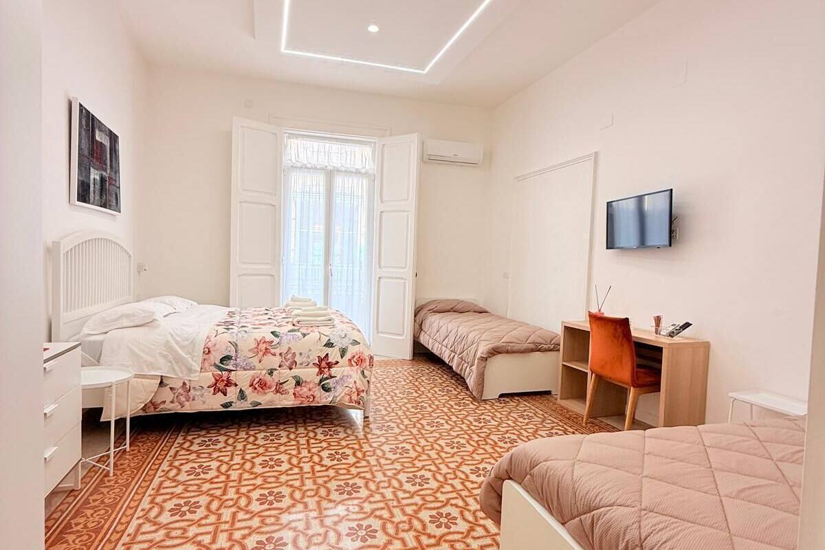 A modern bedroom with a patterned floor, a bed with floral bedding, a desk with a chair, and a TV on the wall.