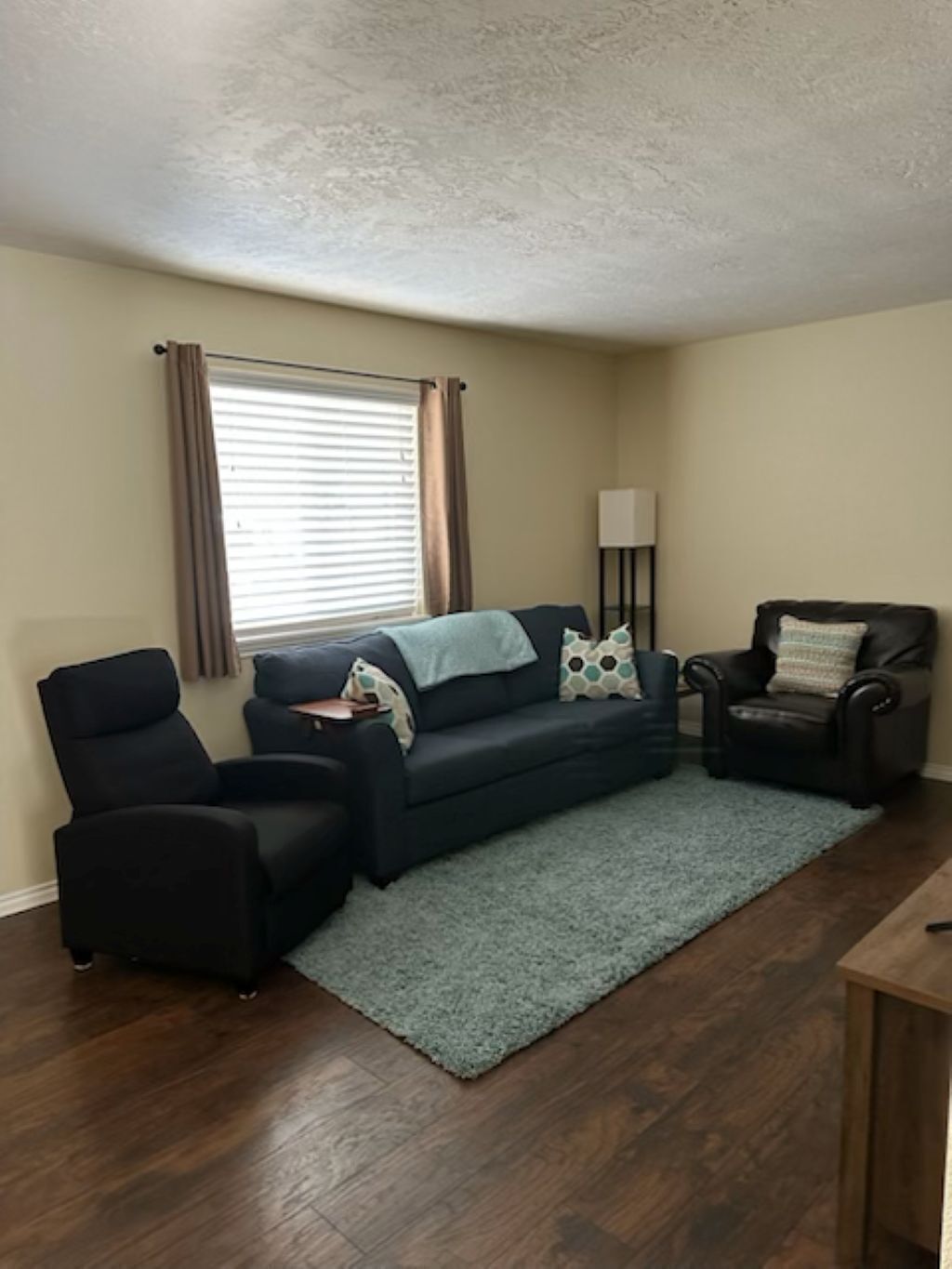 A living room with a dark blue sofa, two black armchairs, a small table, and a floor lamp.