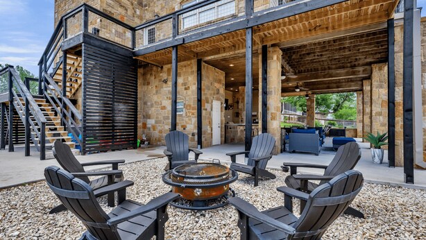 An outdoor patio area with Adirondack chairs, a fire pit, and a stone building with a wooden deck. - Pool, Sandy Beach & Amazing Lake Sunsets, Sleeps 16, Family Retreat + Game Room (Kingsland)