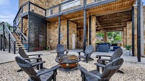 An outdoor patio area with Adirondack chairs, a fire pit, and a stone building with a wooden deck. - Pool, Sandy Beach & Amazing Lake Sunsets, Sleeps 16, Family Retreat + Game Room (Kingsland)