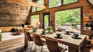 A rustic wooden cabin with a dining area, large windows, and a cozy seating area.