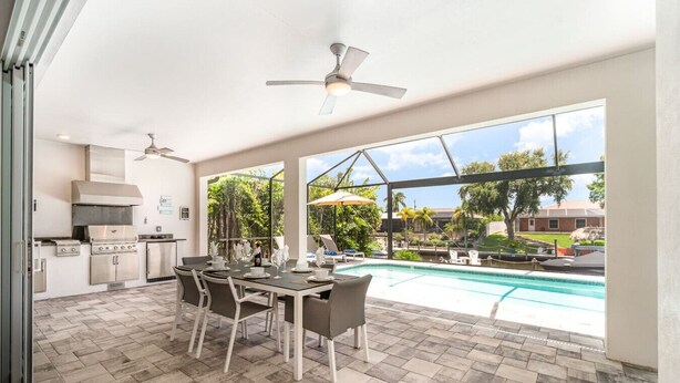 Amplio espacio al aire libre con piscina, mesa de comedor, sillas y zona de cocina con parrilla.