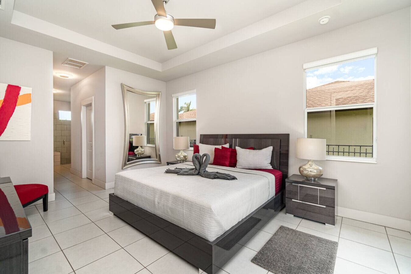 A modern hotel room with a large bed, a ceiling fan, a bedside table with a lamp, and a window with a view of the outside.