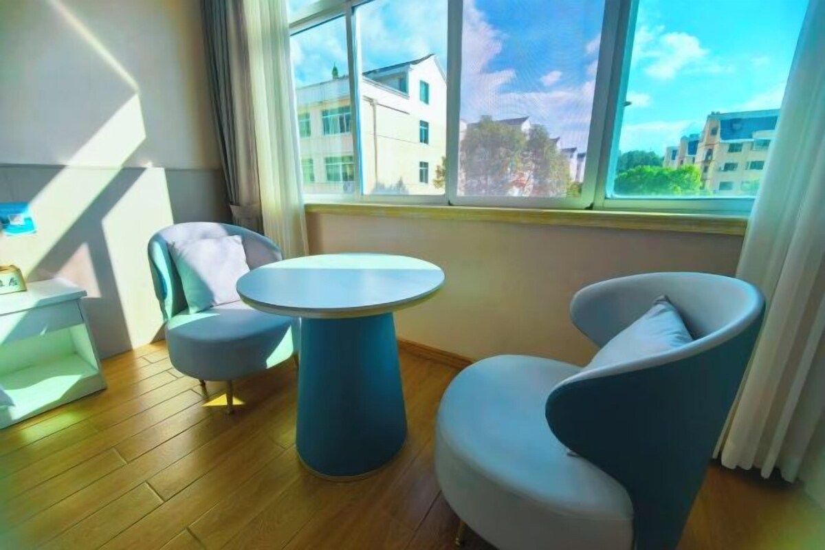 A modern room with a round table and two chairs, a small white cabinet, and a large window with a view of buildings.