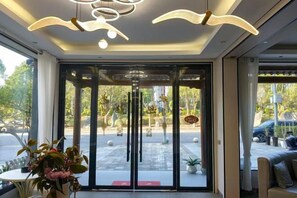 Een hotelentree met een glazen deur, binnenshuis planten en een uitzicht op de straat.