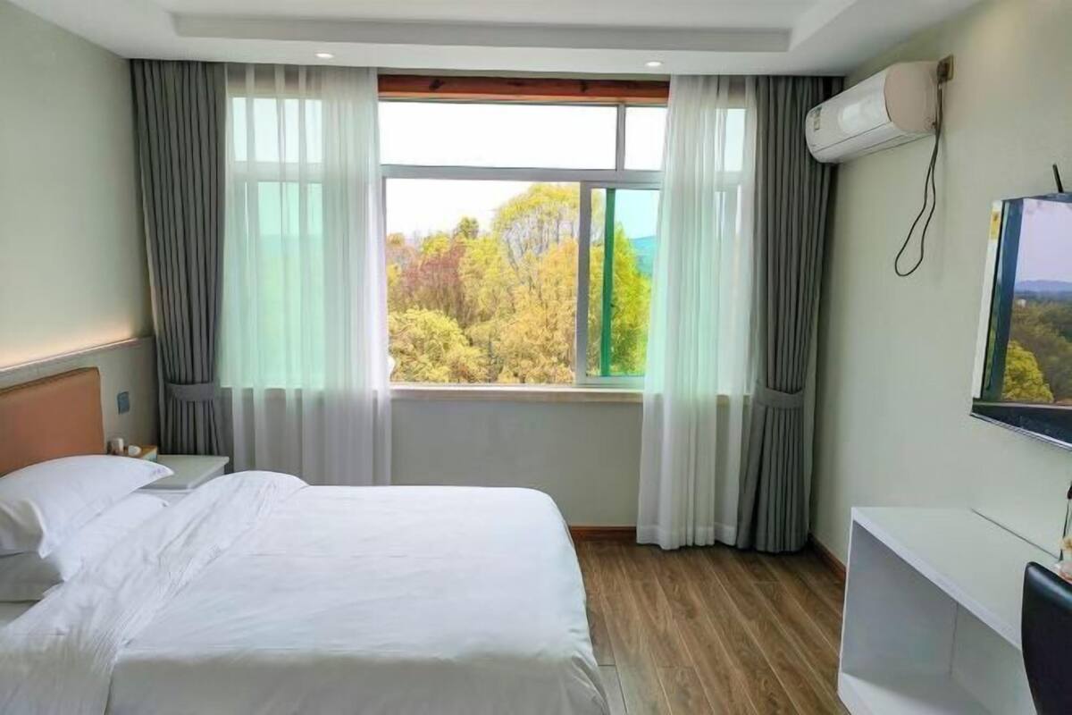 Ein Hotelzimmer mit einem großen Bett, einem Wandfernseher und einem Fenster mit Vorhängen.