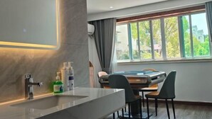 Et moderne badeværelse med et stort spejl, en vask og toiletartikler. Der er et vindue med gardiner og udsigt til grøn vegetation udenfor.