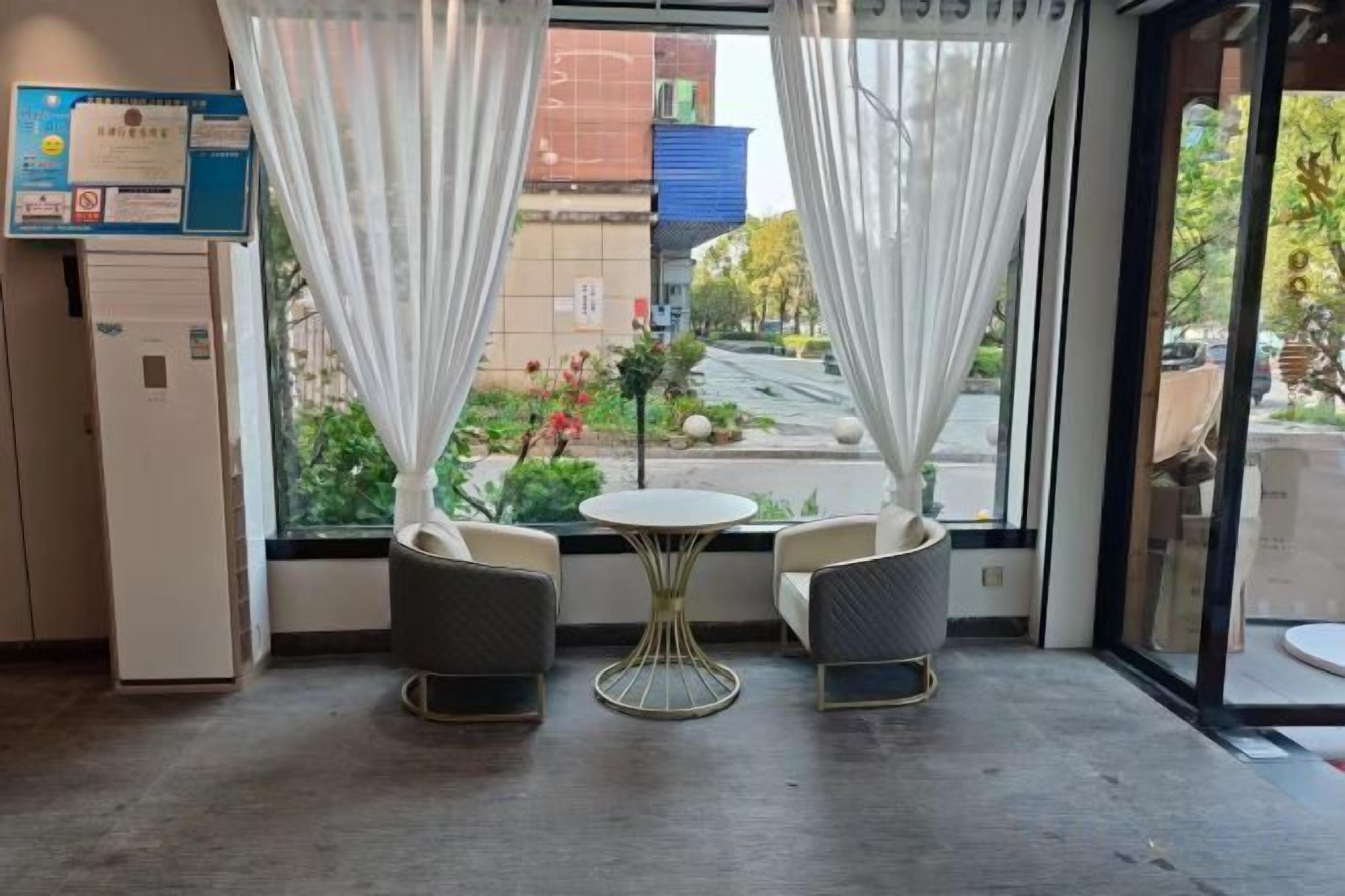 A room with two chairs and a small table, a window with curtains, and a view of the outside.