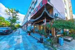 A street view with a building featuring a traditional architectural style, a car parked on the side, and potted plants along the sidewalk. - Wencheng Wufu Farmhouse (Wencheng)