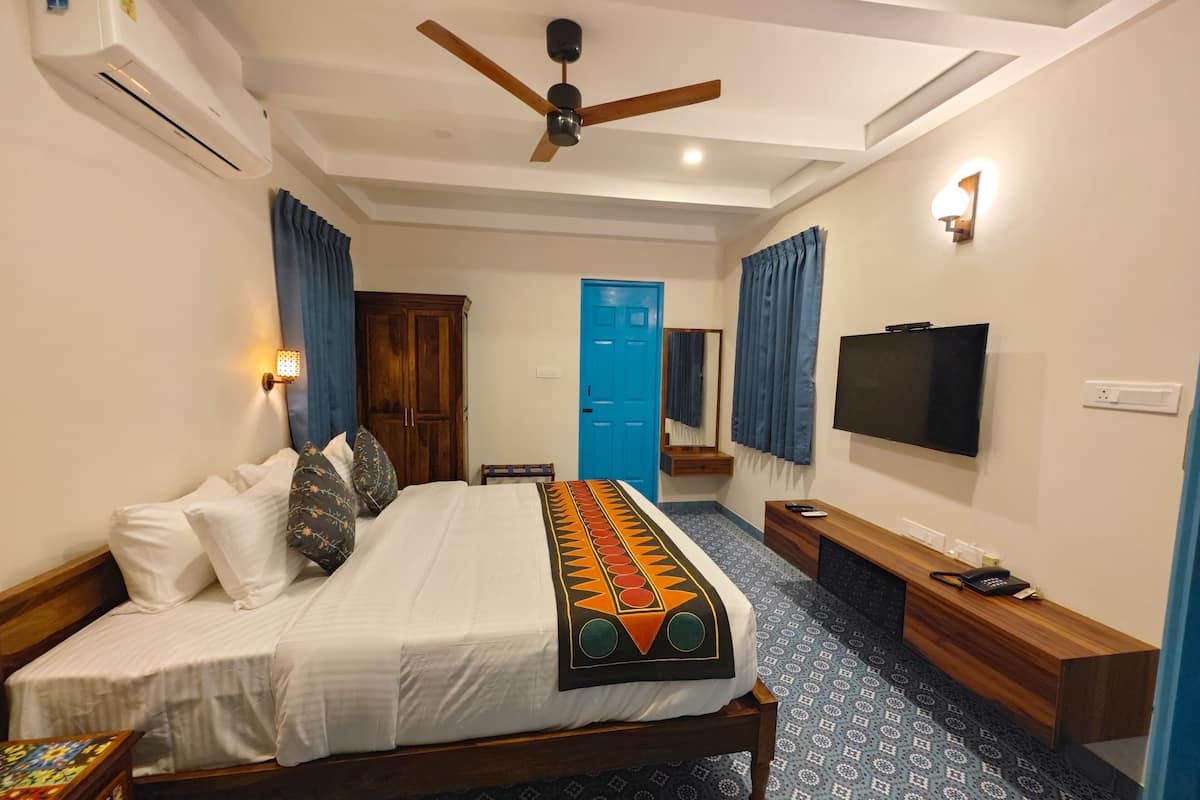 A hotel room with a bed, a ceiling fan, a TV, a desk, and a blue door.
