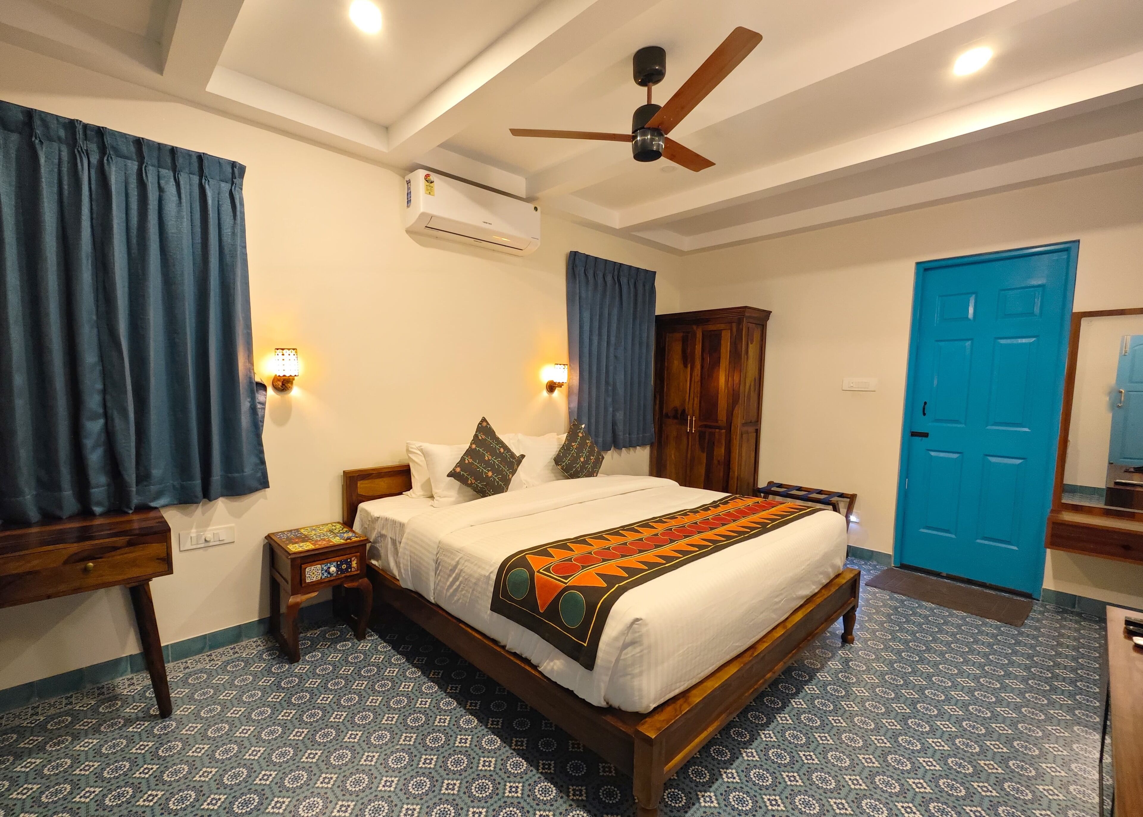 A bedroom with a bed, a ceiling fan, an air conditioning unit, a wardrobe, a blue door, and patterned floor tiles.