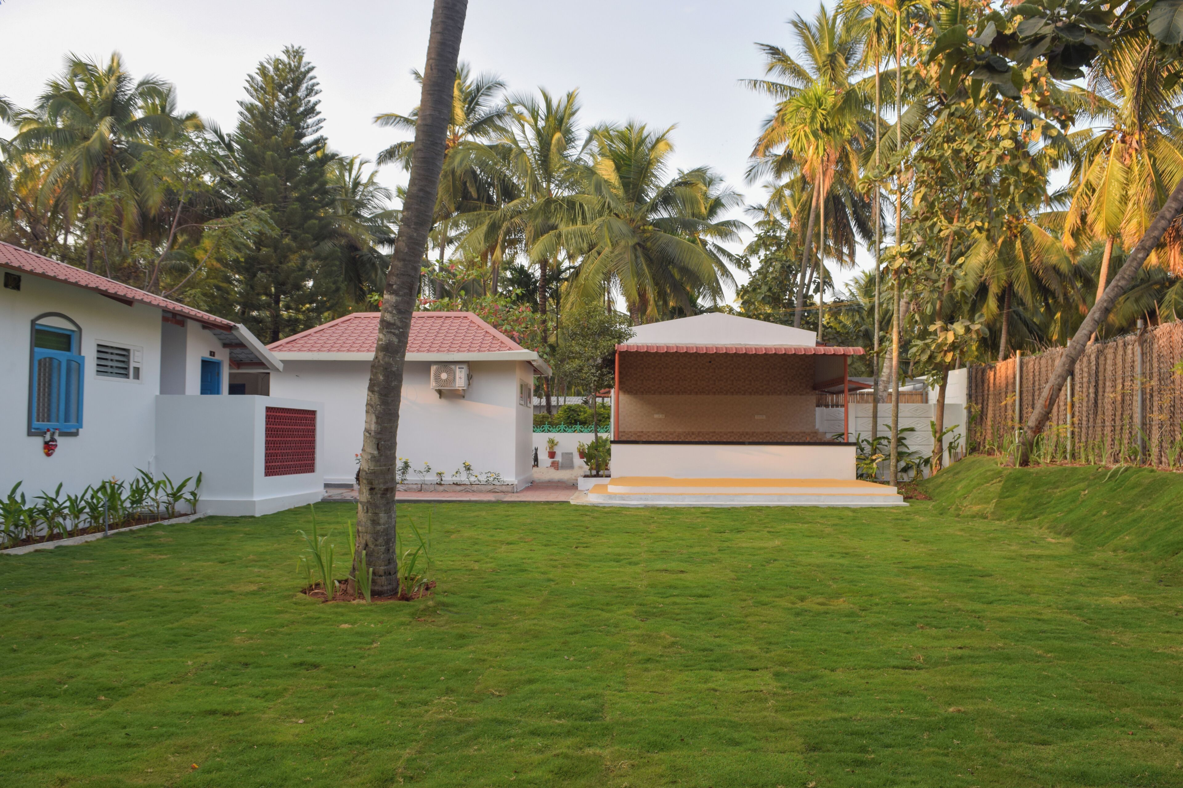 A white building with a red roof and blue doors, surrounded by a well-maintained lawn and palm trees.