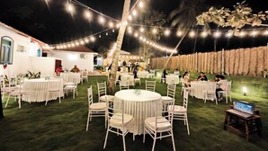 An outdoor event space with round tables and chairs, string lights, and a grassy area. - Ibex Resorts Coimbatore Kakarala (Coimbatore)