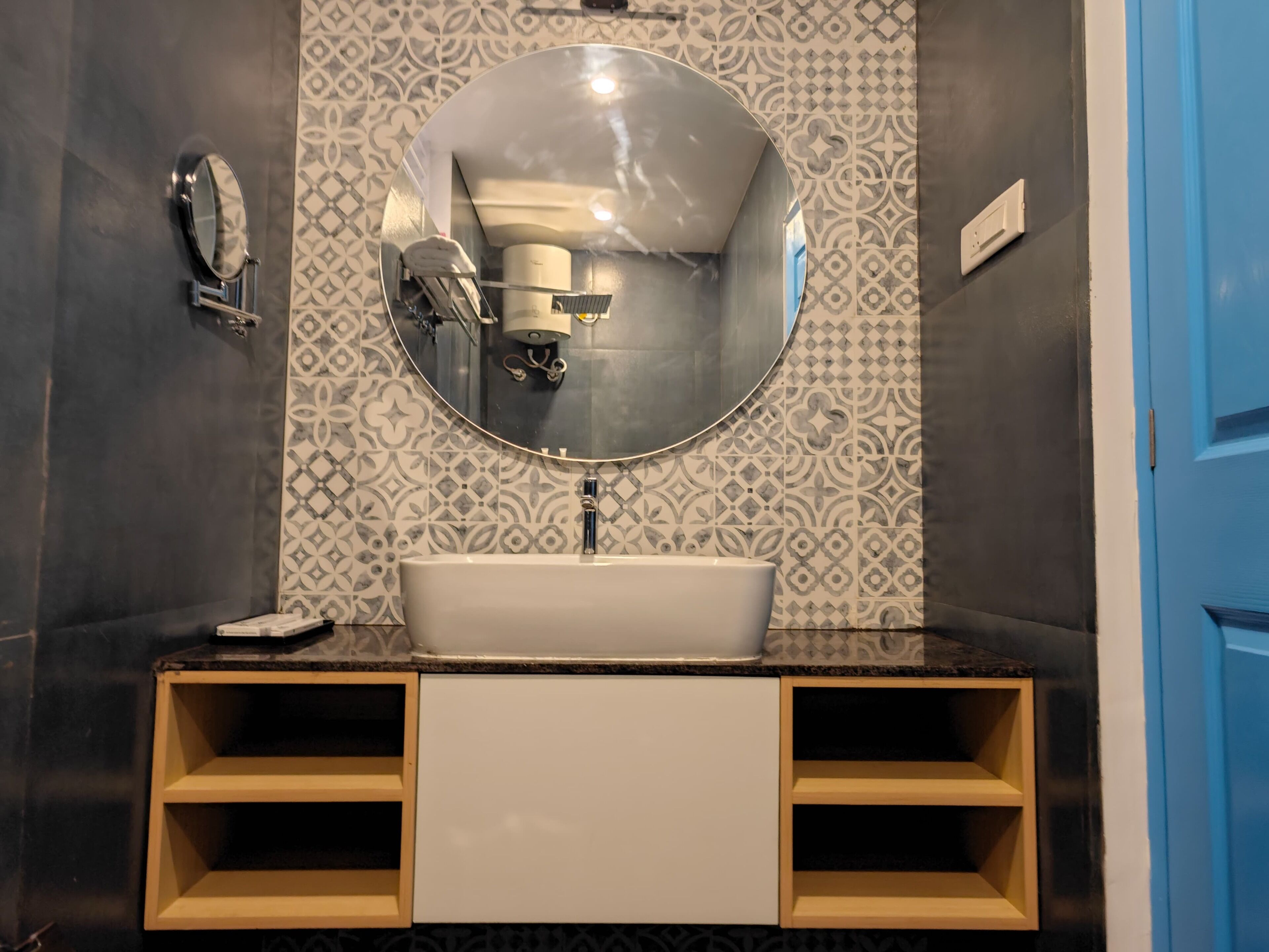 A bathroom with a round mirror, a white sink, and patterned tiles on the walls.