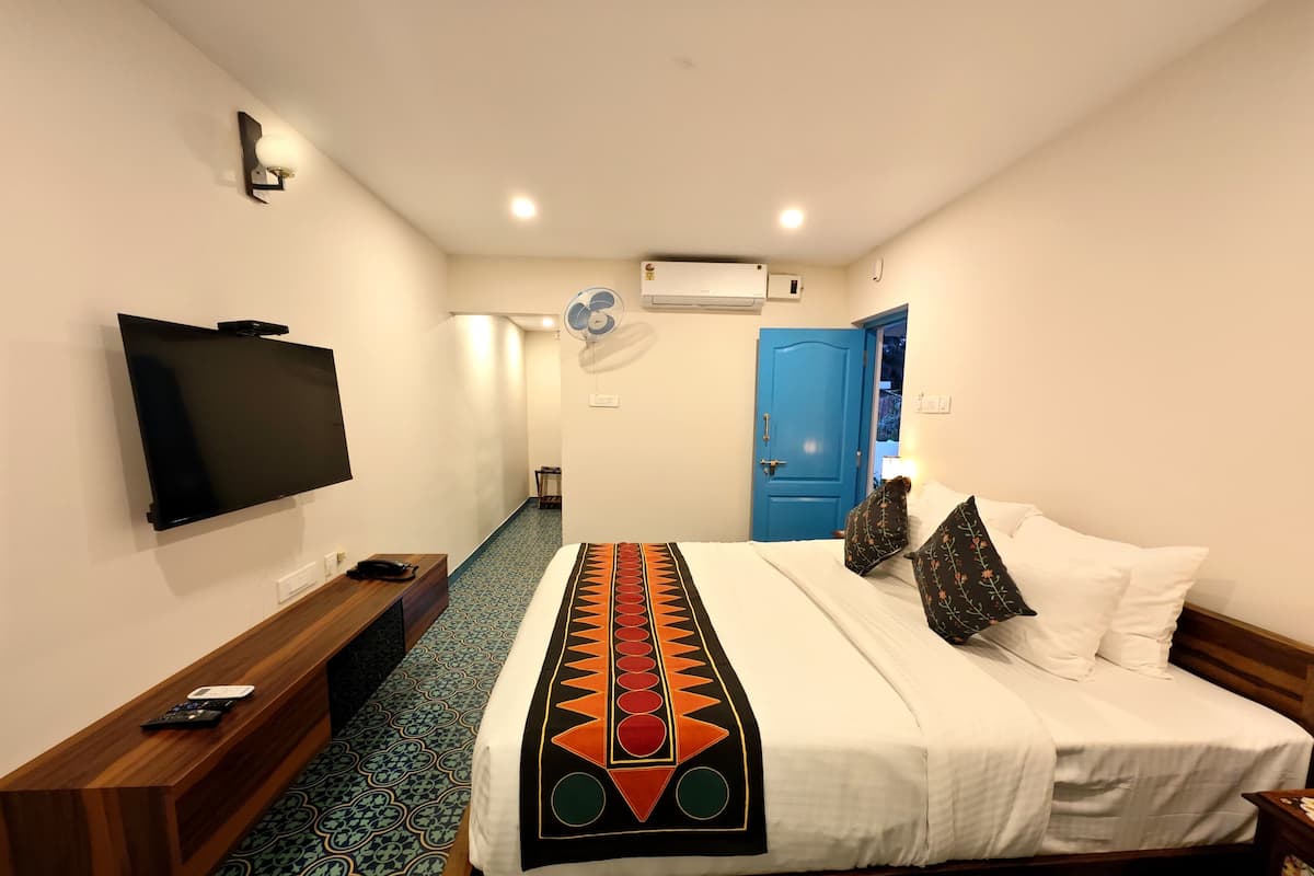A hotel room with a bed, a TV, a desk, and a blue door.