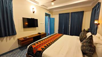 A hotel room with a bed, a TV mounted on the wall, a ceiling fan, and a blue door.