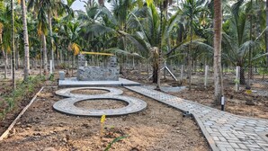 A landscaped garden with a winding pathway, stone structures, and a fenced area with palm trees. - Ibex Resorts Coimbatore Kakarala (Coimbatore)
