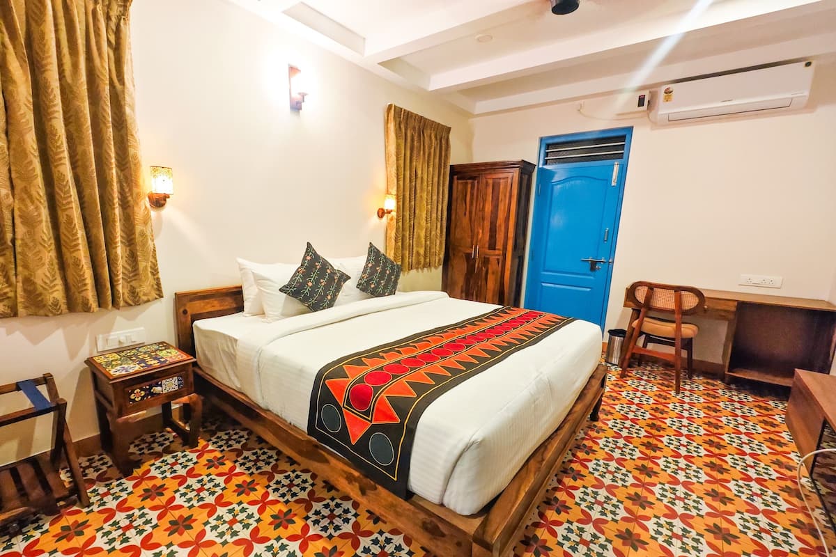 A bedroom with a bed, a desk, a chair, a wardrobe, and patterned flooring.