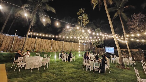 An outdoor event space with string lights, tables, chairs, and palm trees. - Ibex Resorts Coimbatore Kakarala (Coimbatore)