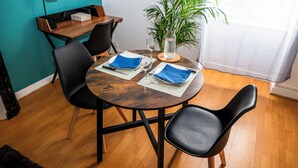 Et spiseområde med et rundt træbord, to sorte stole, en potteplante og et lille træsidebord med en lampe.