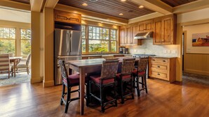 A spacious kitchen with wooden cabinets, a stainless steel refrigerator, and a large island with bar stools. - Charming VT ski retreat with hot tub, pool, fire pit & endless mountain views (Weston)