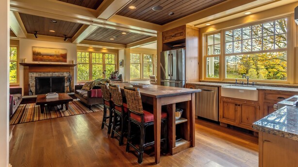 A spacious kitchen with a large island, wooden cabinets, and a built-in oven. There is a dining area with a sofa and chairs, and a fireplace. - Charming VT ski retreat with hot tub, pool, fire pit & endless mountain views (Weston)