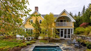 A two-story house with a stone patio and a swimming pool. - Charming VT ski retreat with hot tub, pool, fire pit & endless mountain views (Weston)
