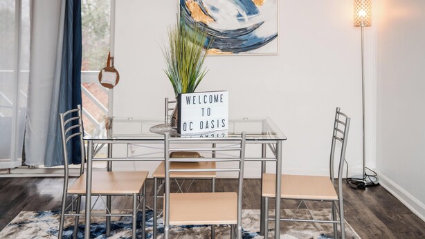 A modern dining area with a glass table, metal chairs, and a welcome sign. - Upscale 2 Queen Beds/2 Bath in Charlotte University Area (Charlotte)