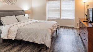 A bedroom with a bed, bedside table, lamp, and a window with blinds. - Upscale 2 Queen Beds/2 Bath in Charlotte University Area (Charlotte)