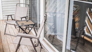 A wooden deck with two chairs and a table, a sliding glass door, and a view of trees and a deck railing. - Upscale 2 Queen Beds/2 Bath in Charlotte University Area (Charlotte)
