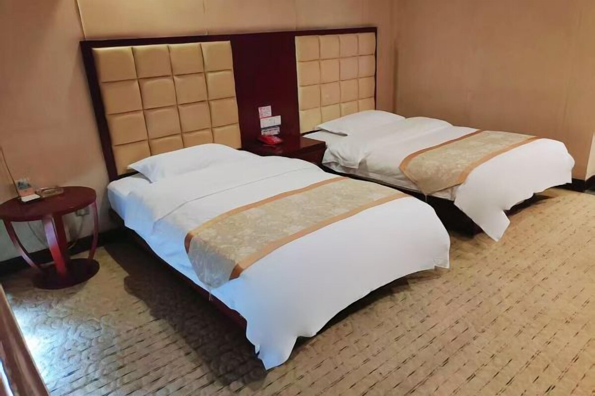 A hotel room with two beds, a wooden headboard, a small round table, and a carpeted floor.