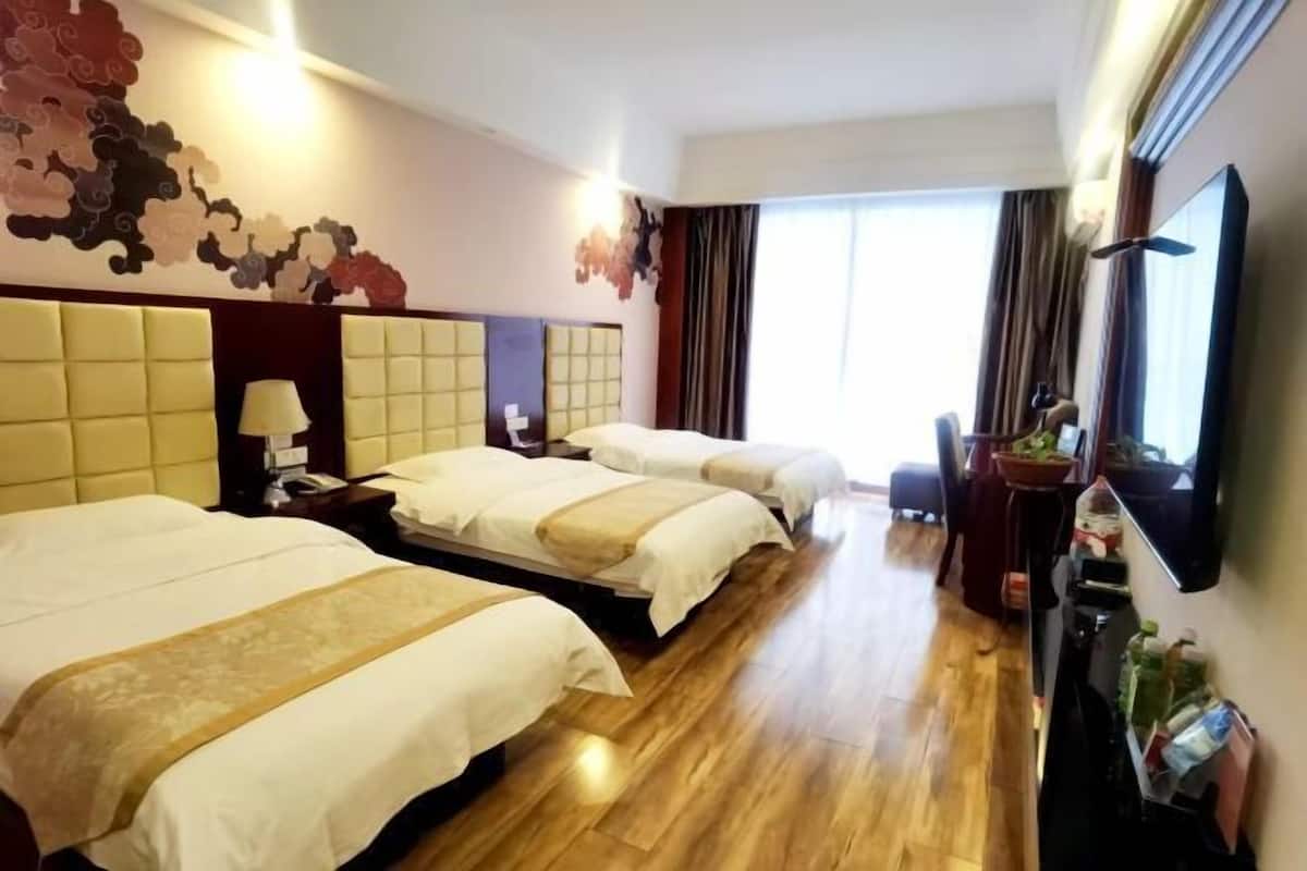 Une chambre d’hôtel avec trois lits, une télévision, un bureau et une grande fenêtre avec des rideaux.