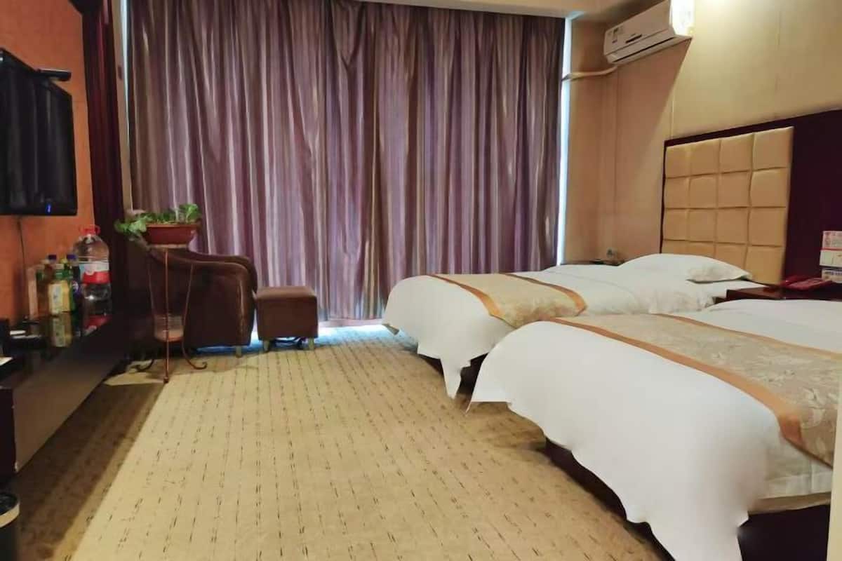 Une chambre d’hôtel avec deux lits, un bureau, une chaise, une plante en pot et un rideau.