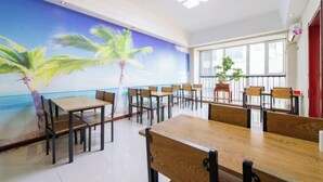 Un comedor con mesas y sillas de madera, un mural con palmeras en la pared y un amplio ventanal que proporciona luz natural.