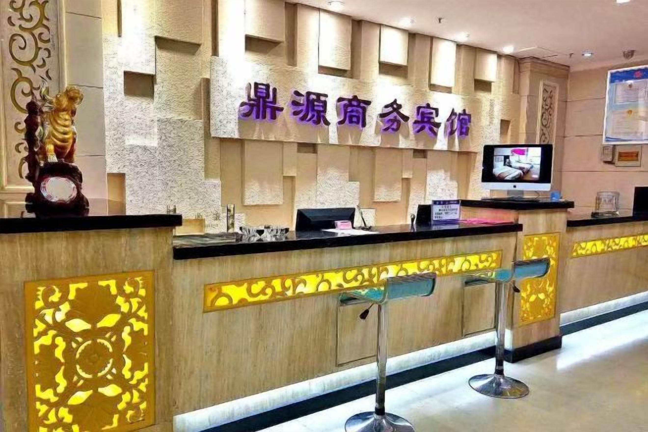 Una recepción con pantalla digital, un muro decorativo y dos taburetes de bar.