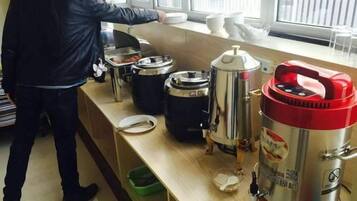 Disposición de bufé con varios recipientes de comida y una persona sirviendo.