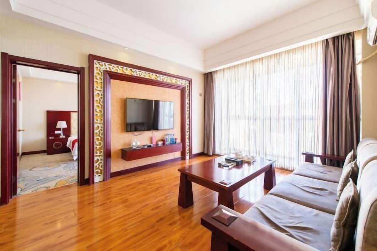 Une chambre d’hôtel avec un plancher en bois, un canapé, une télévision et une fenêtre avec des rideaux.