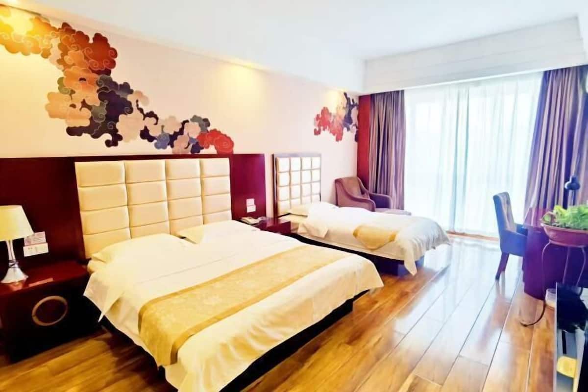 Une chambre d’hôtel avec deux lits, un plancher en bois, un mur d’accent rouge et une grande fenêtre avec des rideaux.