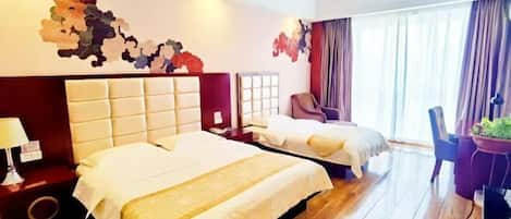 A hotel room with two beds, a wooden floor, a red accent wall, and a large window with curtains.