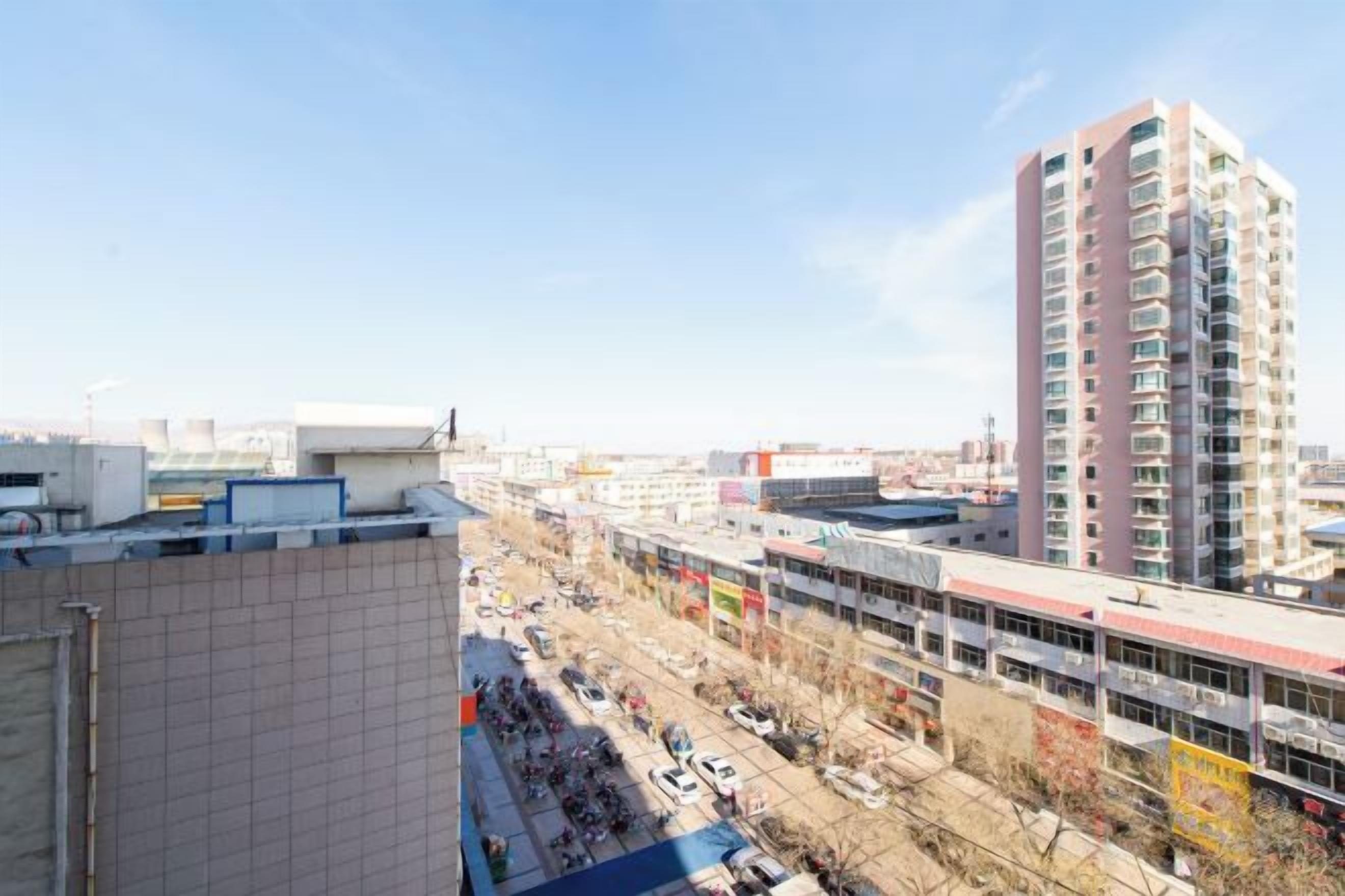Un immeuble de grande hauteur, avec de nombreux étages, une rue animée en contrebas et un ciel dégagé.