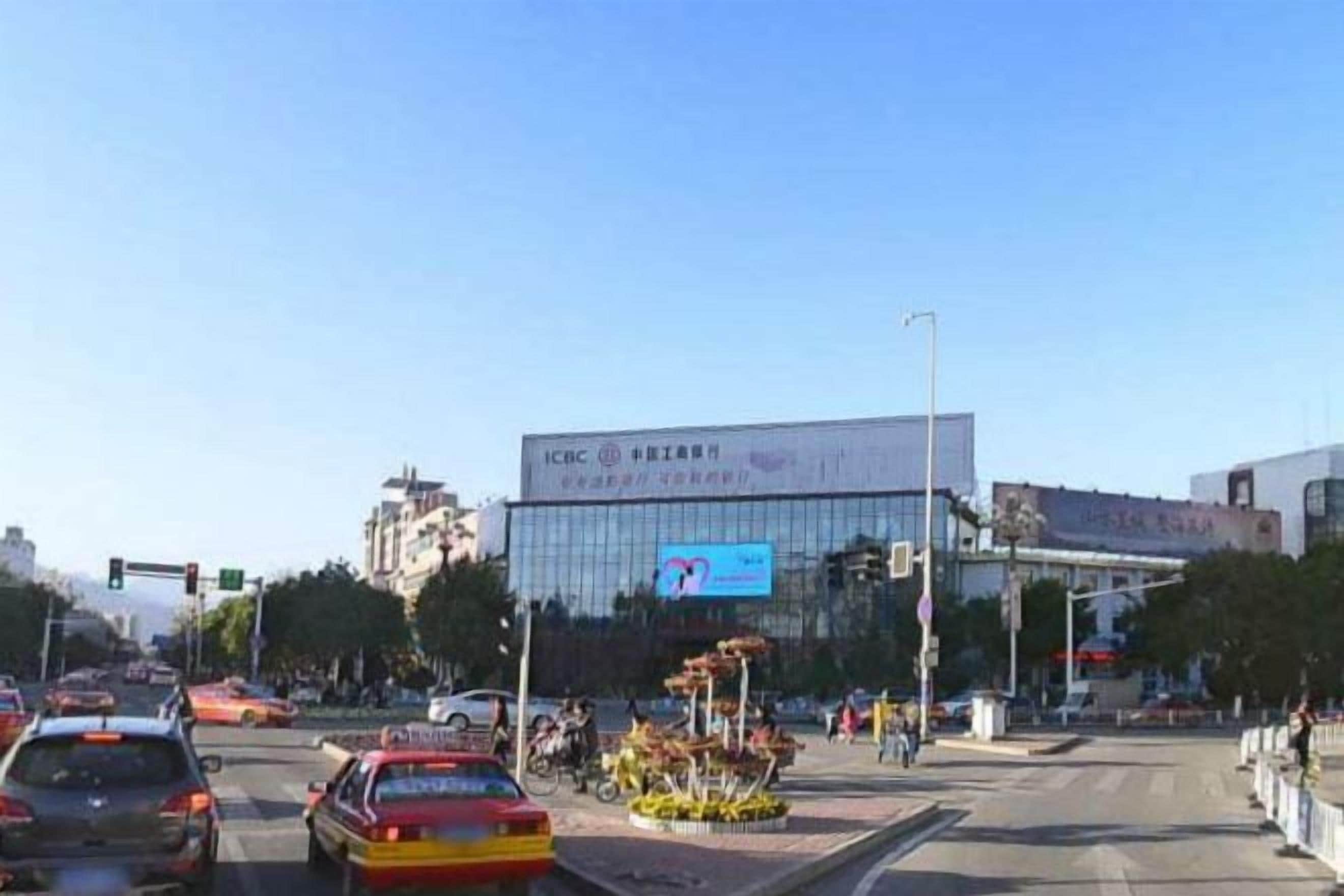 A busy intersection with a modern building featuring a large digital display.