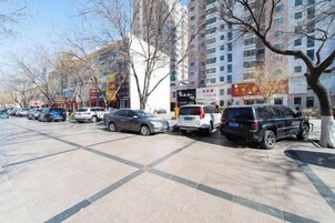 A parking lot with multiple cars parked along a sidewalk, adjacent to a building with signage.