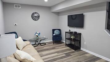 Una sala de estar moderna con un sofá color beige, una mesa de centro de vidrio, un sillón azul y un televisor instalado en la pared.
