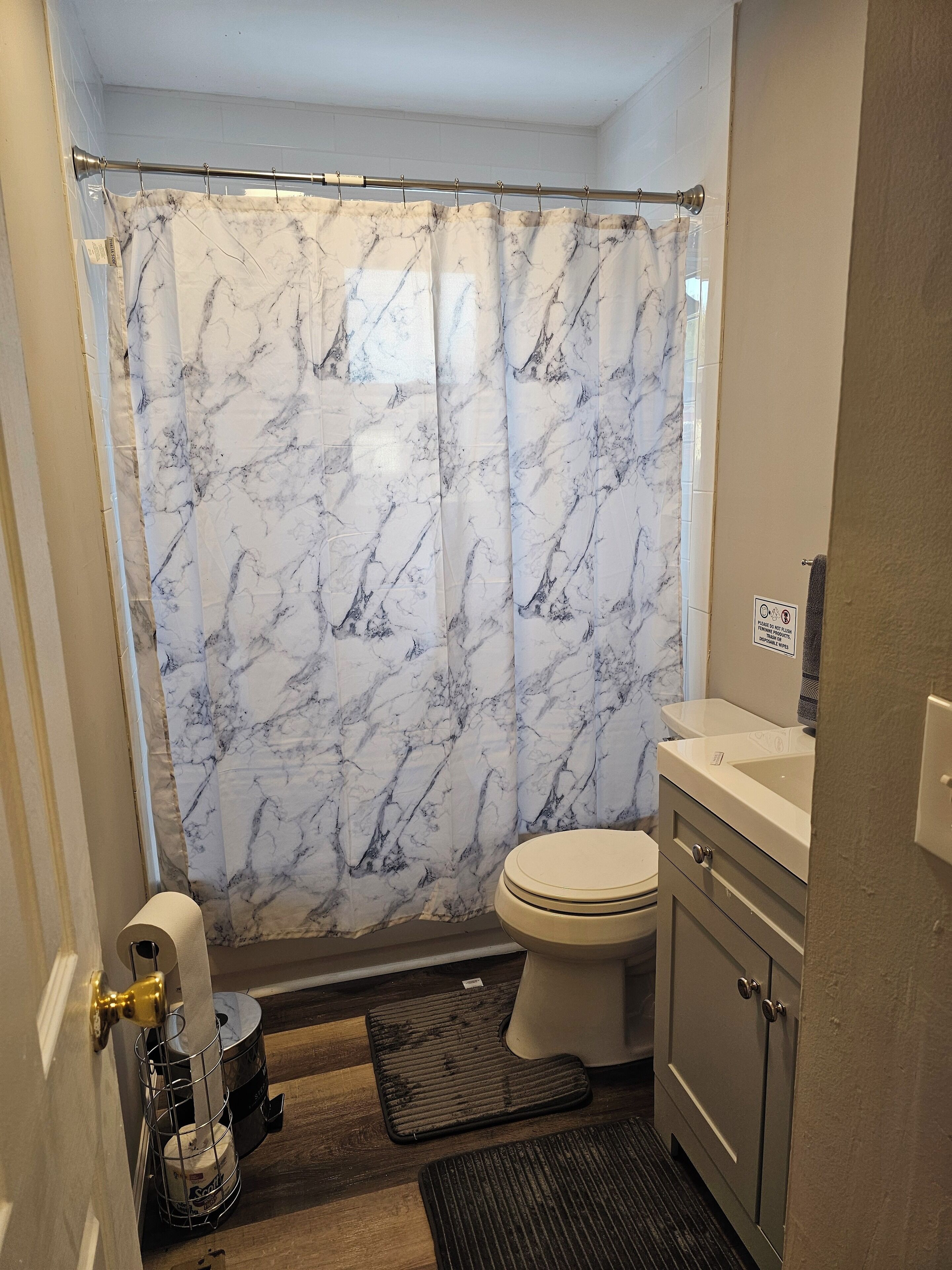 A bathroom with a marble-patterned shower curtain, a toilet, a sink, and a door with a towel rack.