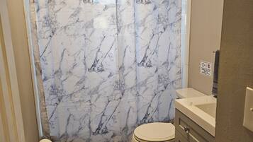 A bathroom with a marble-patterned shower curtain, a toilet, a sink, and a door with a towel rack.