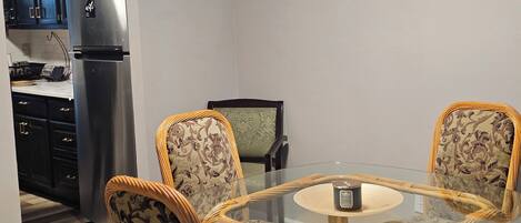 A dining area with a glass table and four chairs with patterned upholstery.