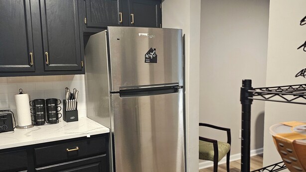 A modern kitchen with dark cabinets, a stainless steel refrigerator, and a wooden floor. - Family-Friendly 4BR Home in Elkton - AC, High-Speed WiFi & Relaxing Vibes (Elkton)